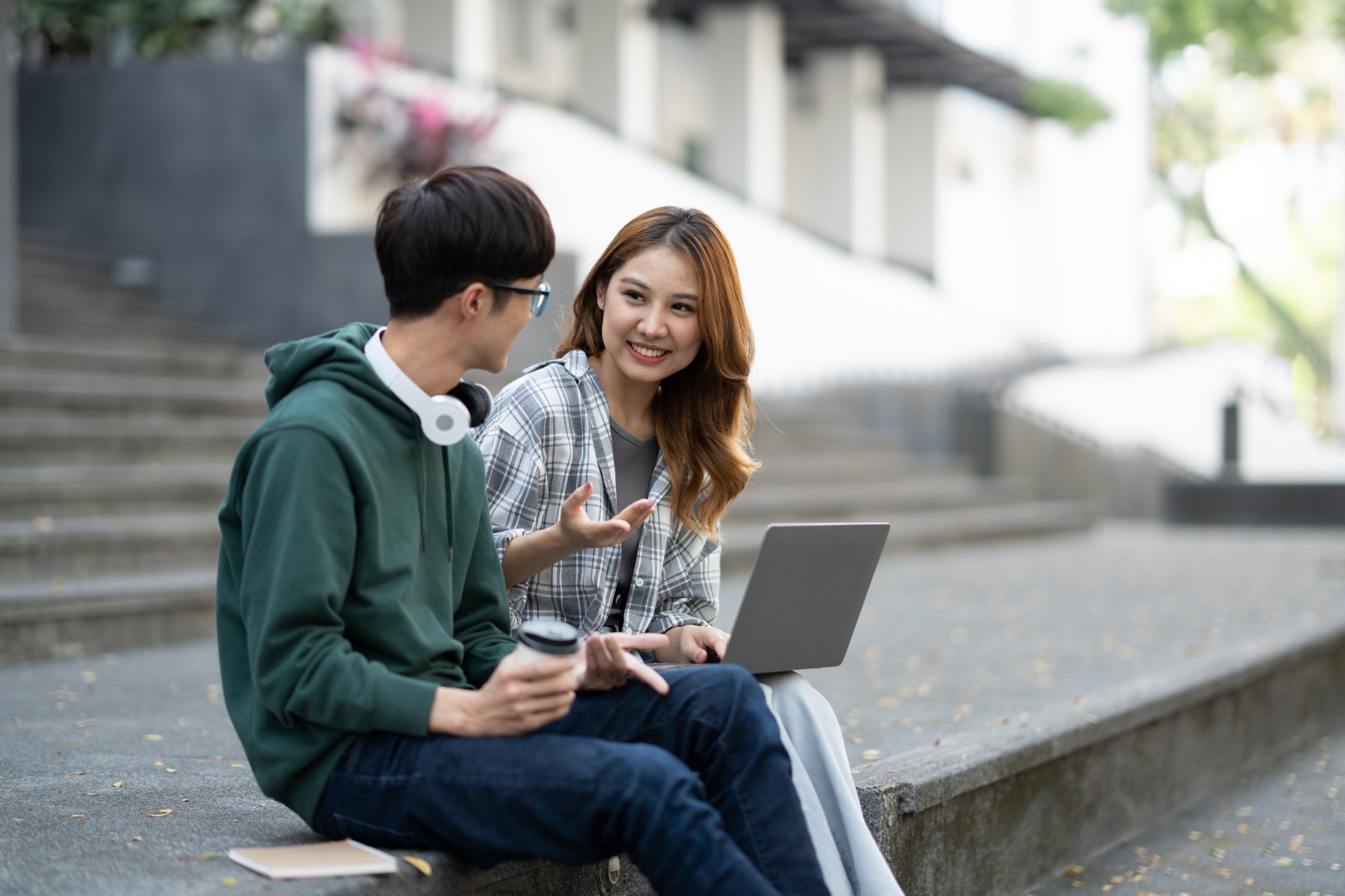 Young Asian college students reading books, studying on laptop, preparing for exam or working on gro